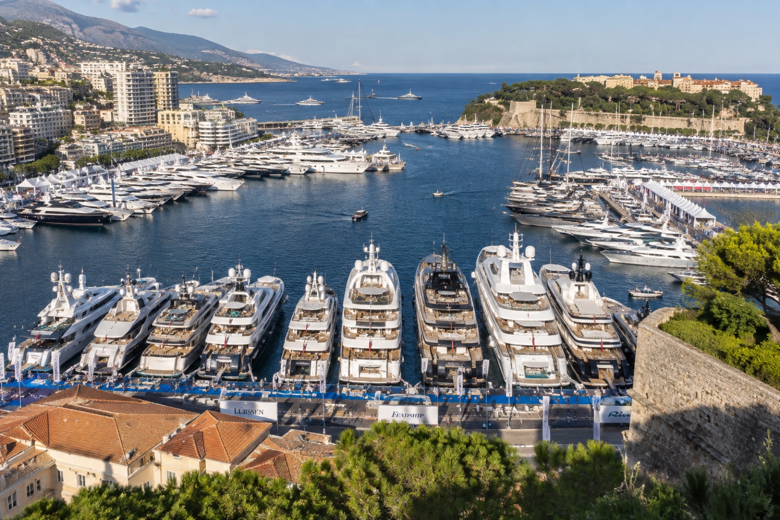 Port Hercule in Monaco during the yacht show, superyachts moored stern-to along the quays, seen from the Rock in afternoon sunlight