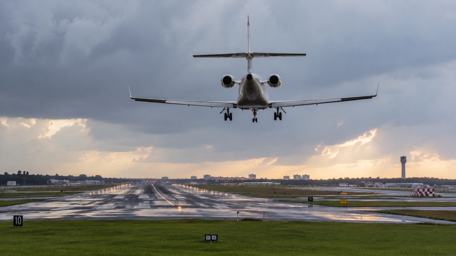 A business jet on final approach over a wet runway as the sky clears after the storm