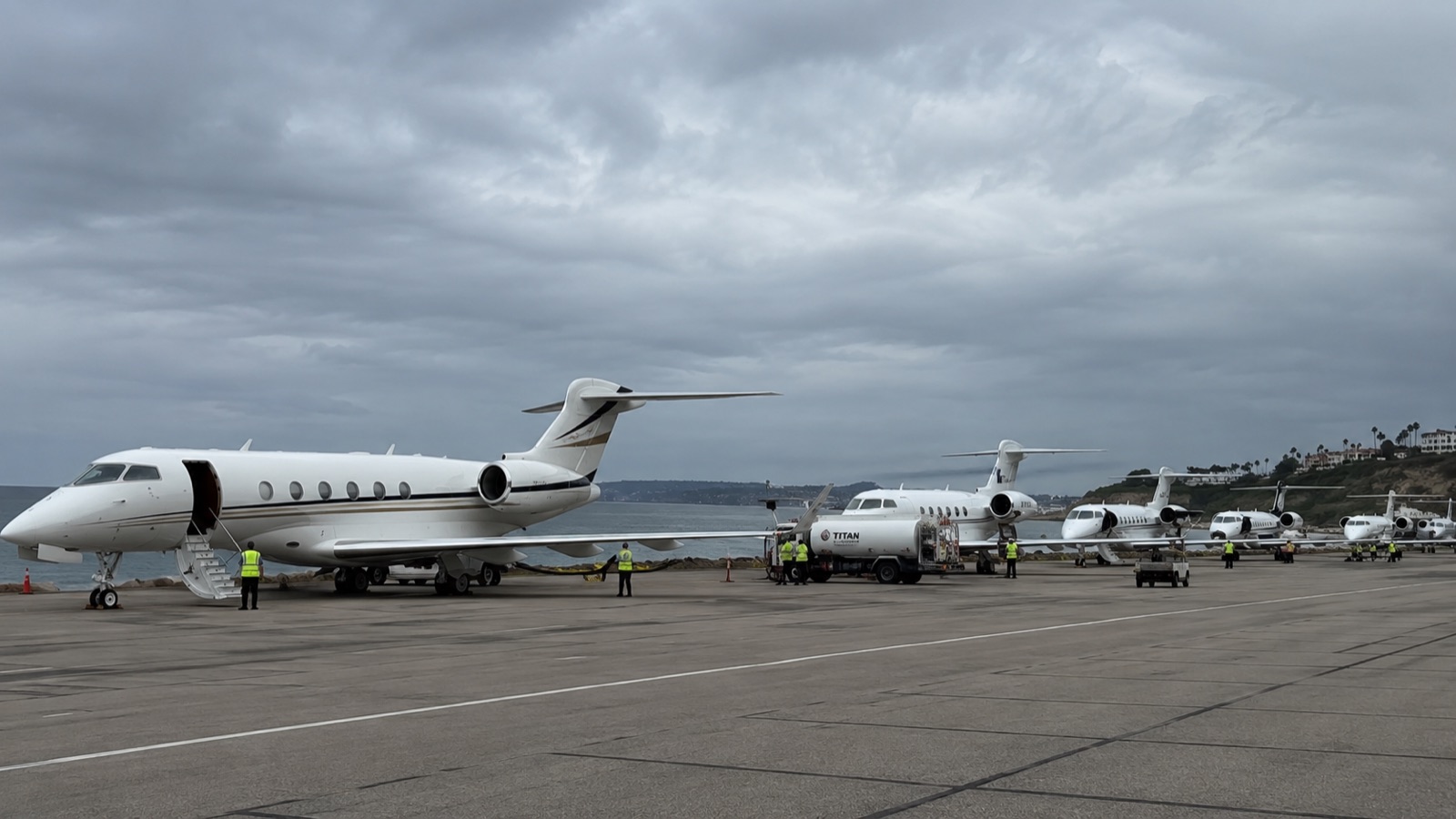 A line of business jets on a coastal ramp under a heavy grey sky