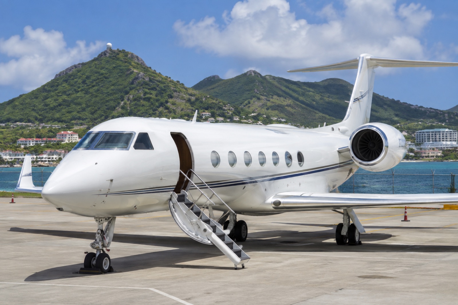 A large-cabin business jet on the general aviation ramp at St. Maarten, green hills and the lagoon behind it in bright sun