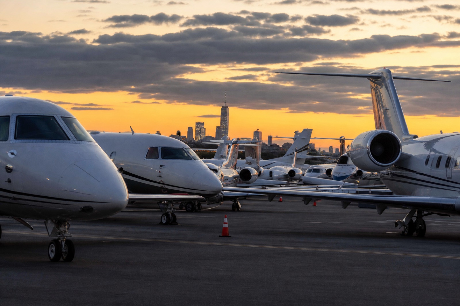 Business jets parked wingtip to wingtip on a crowded FBO ramp at dusk